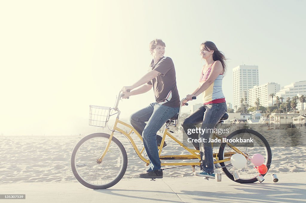 Couple riding tandem bike on beach boardwalk