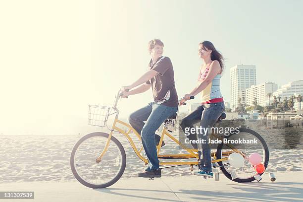 couple riding tandem bike on beach boardwalk - bicycle tandem stock pictures, royalty-free photos & images
