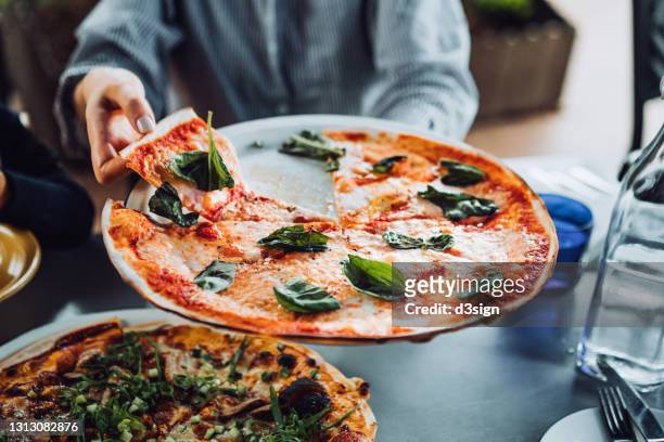 close up of young asian woman getting a slice of freshly made pizza. enjoying her meal in an outdoor restaurant. italian cuisine and culture. eating out lifestyle - cibo italiano foto e immagini stock