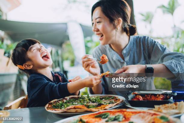 joyful young asian mother and lovely little daughter enjoying pizza lunch in an outdoor restaurant while mother serving meatballs and bolognese to daughter. family enjoying bonding time and a happy meal together. family and eating out lifestyle - meal ストックフォトと画像