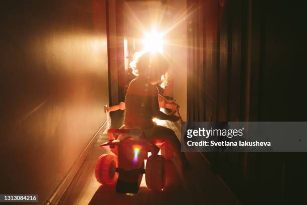 a little girl during a lockdown due to сovid-19 plays at home - drives a toy car along the corridor in the sunset rays of the sun from the window - toddler in car foto e immagini stock