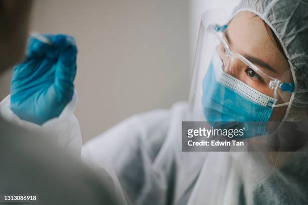 asiatische chinesische ärztin mit psa, die nasenabstrich aus dem coronavirus-test des patienten nimmt. medizinische rind in schutzsuite unter einem tupfer für corona-virus-test, potenziell infizierte frau - asian man suite stock-fotos und bilder