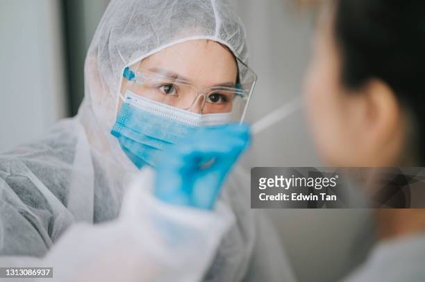 asiatische chinesische ärztin mit psa, die nasenabstrich aus dem coronavirus-test des patienten nimmt. medizinische rind in schutzsuite unter einem tupfer für corona-virus-test, potenziell infizierte frau - coronavirus stock-fotos und bilder