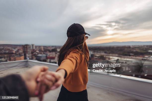 follow me concept, beautiful young woman standing on rooftop and holding boyfriends hand - fashion model couple stock pictures, royalty-free photos & images