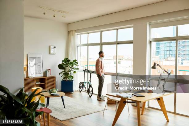 man with hands in pockets looking through window - window man out stock pictures, royalty-free photos & images