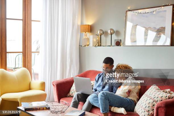 woman leaning on man using laptop in living room - young man laptop couch photos et images de collection