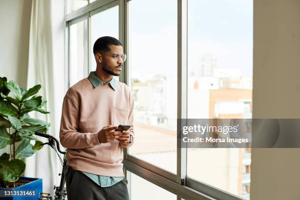 contemplated man with phone looking through window - observar imagens e fotografias de stock