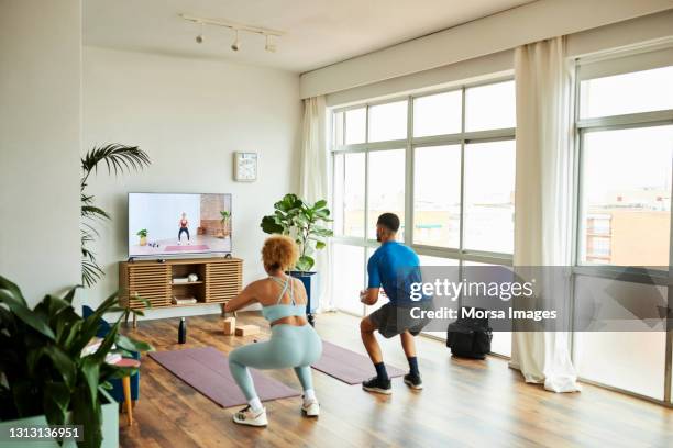 young couple practicing squats in living room - agachar se imagens e fotografias de stock