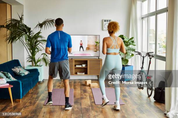 couple watching online exercise class at home - net sports equipment foto e immagini stock