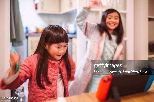 lovely little sisters in their pyjamas playing video game at home joyfully - handheld video game stock pictures, royalty-free photos & images