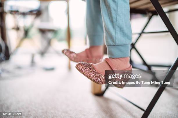 close-up of little girl’s legs in a pair of glittery shoes & pyjamas under the table at home - girl sitting on floor stock-fotos und bilder