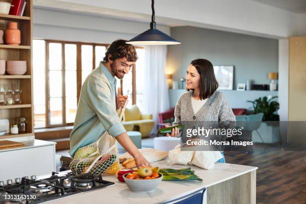 smiling couple unpacking vegetables in kitchen - couple kitchen stockfoto's en -beelden