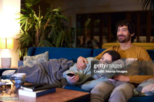 happy couple watching tv in living room at home - couple couch imagens e fotografias de stock