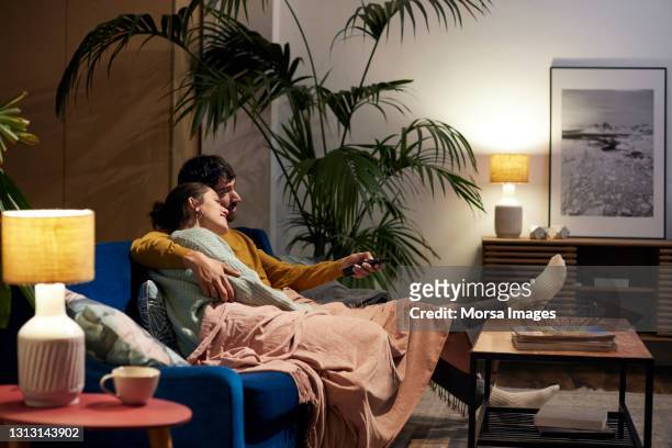 mid adult couple watching tv in living room - sofa stock-fotos und bilder
