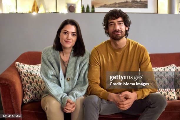 smiling mid adult couple sitting on sofa at home - couple portrait fotografías e imágenes de stock