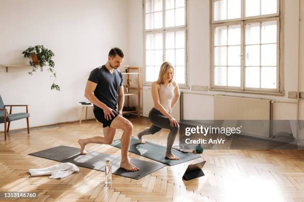 active couple lunging in their spacious living room - couple doing yoga stock pictures, royalty-free photos & images