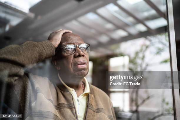 worried senior man looking through the window at home - patient bad news stock pictures, royalty-free photos & images