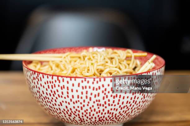 a plate with some chopsticks on top full of noodles with a wooden table in the background - ramen noodles stock pictures, royalty-free photos & images