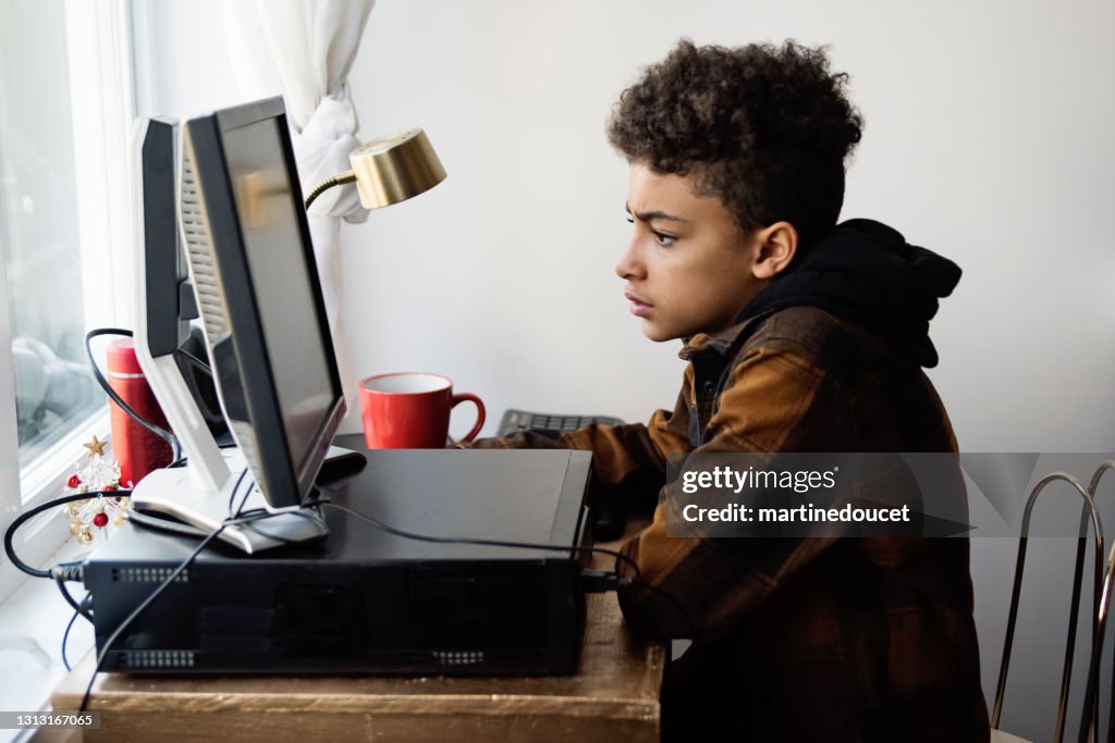 Preteen boy homeschooling on the family desk computer.