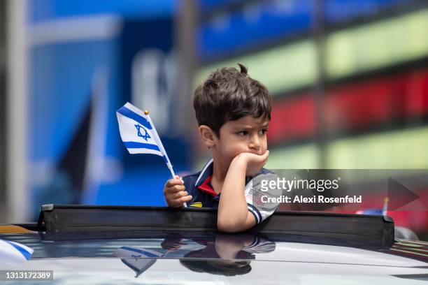 Liam Sher stands out of a car's sunroof waving Israeli flags during a car parade marking Israel’s 73rd Yom Ha’Atzmaut amid the coronavirus pandemic...