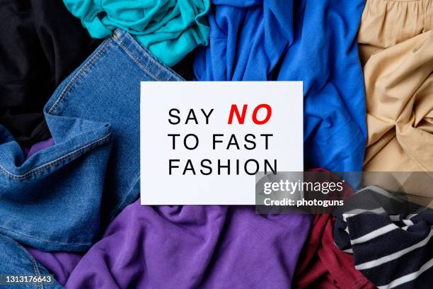 Say NO to fast fashion sign on white paper over heap of female clothes