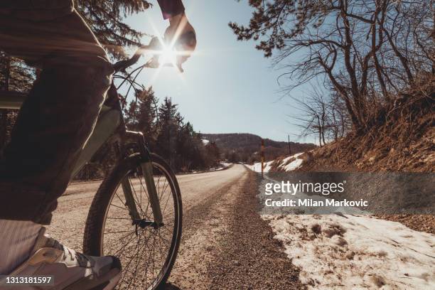 ein männlicher rennradfahrer fährt eine von wald umgebene bergstraße. ein schöner winterlich erweiterlich tag für junge radfahrer zu fahren und in der natur zu bleiben. gesunde lebensweise. - winter triathlon stock-fotos und bilder
