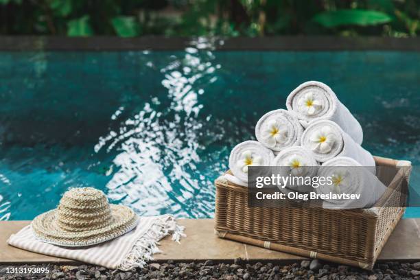 set of rolled white beach towels in wicker box and straw hat on poolside, decorated with tropical  flowers - bali spa stock pictures, royalty-free photos & images