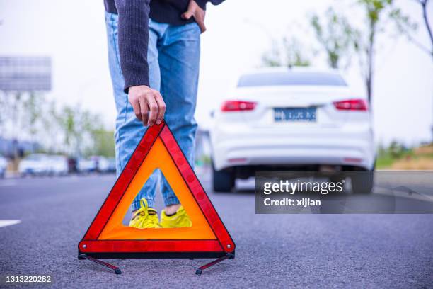 mann setzt rotes warndreieck - roadside assistance stock-fotos und bilder