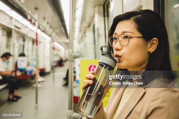 asian businesswoman drinking water from a reusable water bottle in the subway - reusable stock pictures, royalty-free photos & images
