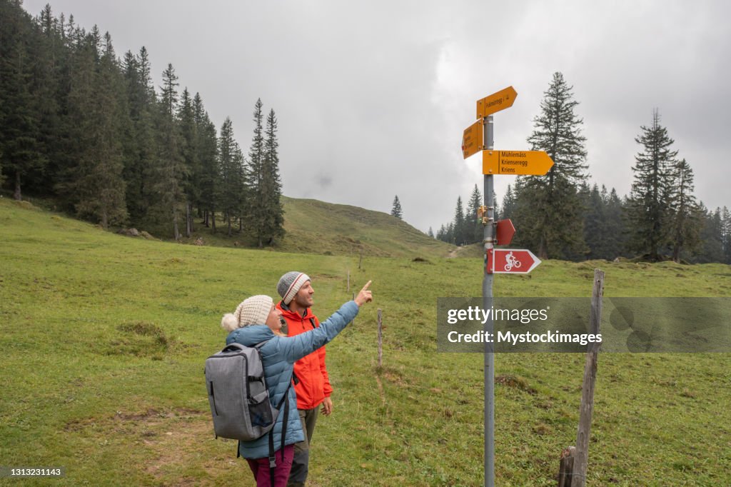 Drone view of couple hiking on mountain trail, stop to look at directional signs