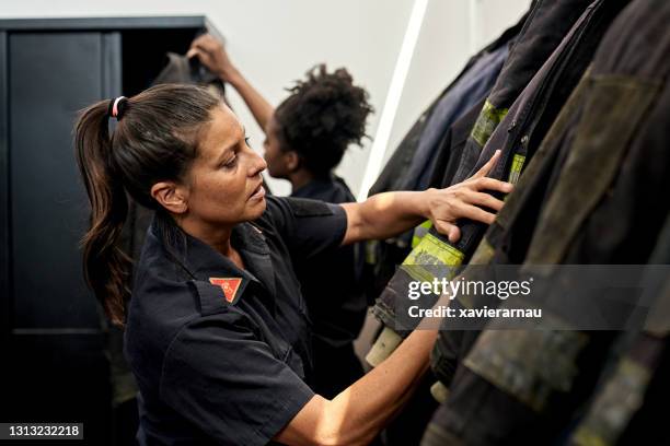 bombeiros do sexo feminino médio se vestindo para chamada de emergência - roupa a prova de fogo - fotografias e filmes do acervo