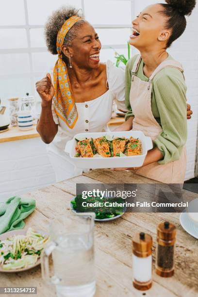 proud mum cheers on daughter after she prepares and presents a salmon meal - cooking fish stock pictures, royalty-free photos & images