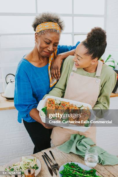 mum rests her arm on daughters shoulder and looks proud as her daughter shows her a salmon meal she has just prepared - mother congratulating stock pictures, royalty-free photos & images