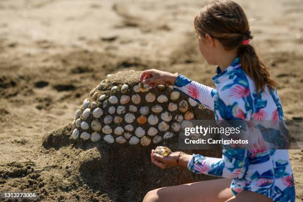 girl sitting on the beach building a sand sculpture with seashells, ireland - sand sculpture stockfoto's en -beelden