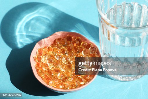 Vitamin D Capsules Next The Glass Of Water On Blue Background Vitamin D Capsules Next The Glass Of Water On Blue Background