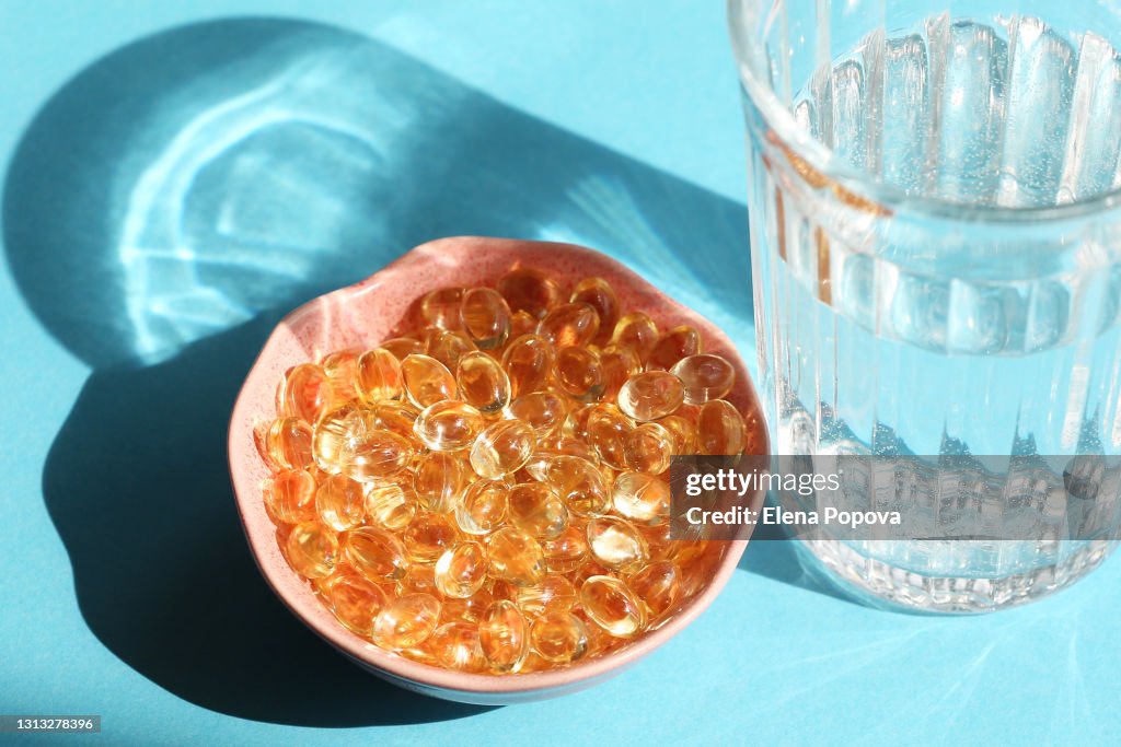 Vitamin D Capsules Next The Glass Of Water On Blue Background