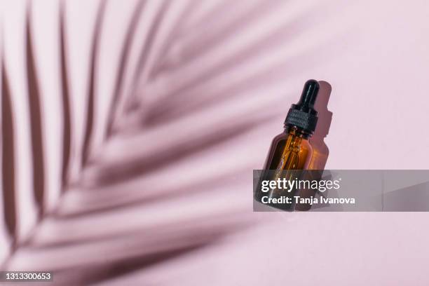 cosmetic glass bottle with pipette on a pink background with shadow of tropical leaf. flat lay, top view. - palmen schatten stock-fotos und bilder