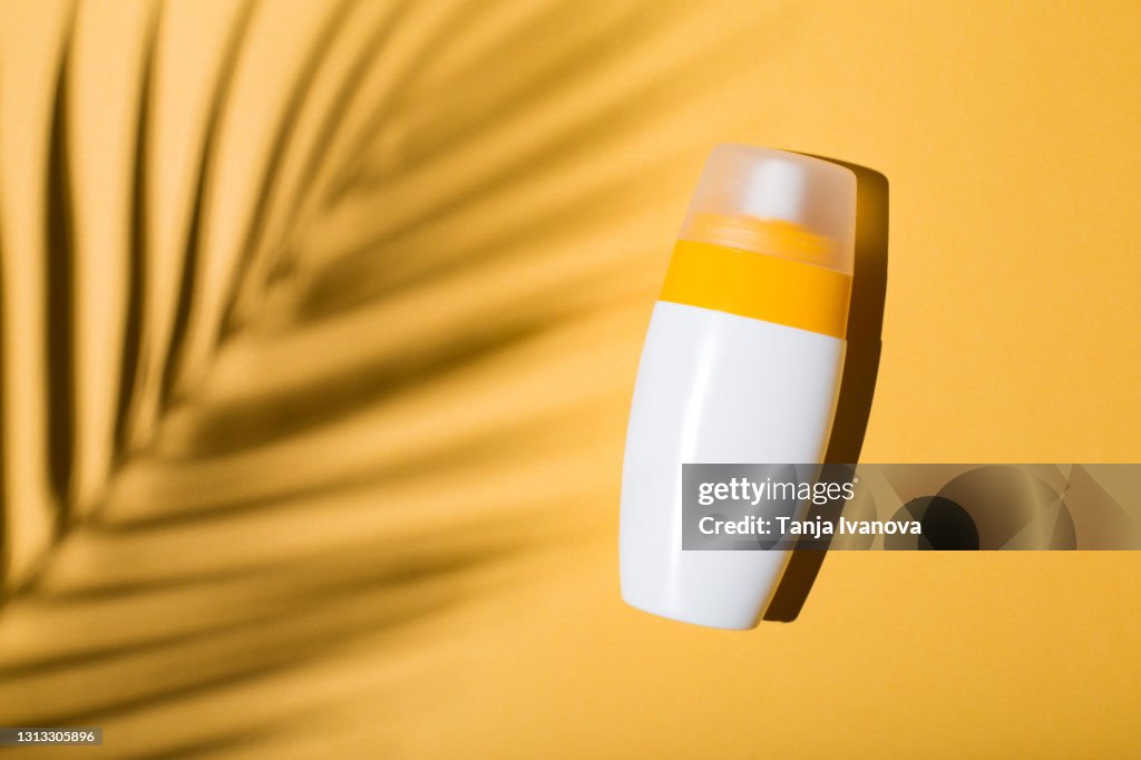 Sunscreen on a yellow background with shadow of tropical leaf. Flat lay, top view.