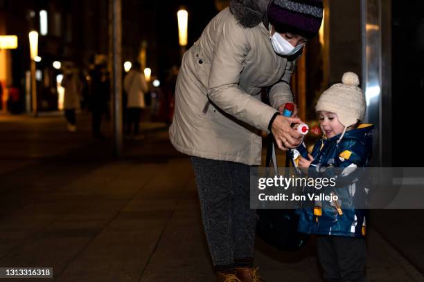 a mother with a mask giving her child a device to blow and make bubbles. they both wear wool hats and it's nighttime. - skater boy hair stock pictures, royalty-free photos & images