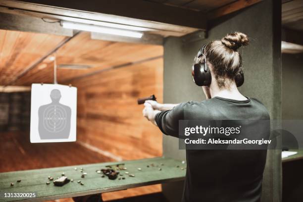 modern male with hair bun taking a shot with gun on target at gun range - gun stock pictures, royalty-free photos & images