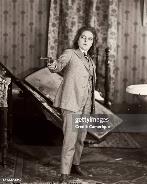 1910s 1920s Terrified Actor Woman Dressed As Man In Three Piece Suit Pointing A Gun Silent Movie Still.