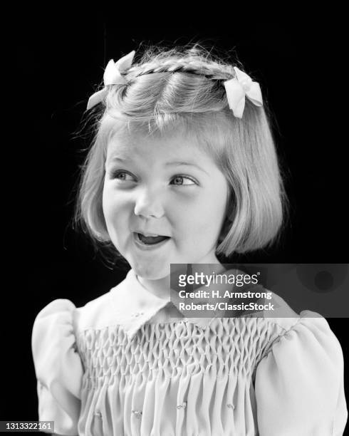 1940s Smiling Cute Blond Girl Looking Off To Side With Mischief In Eyes Bows And Braid In Hair And Smocking On Dress .