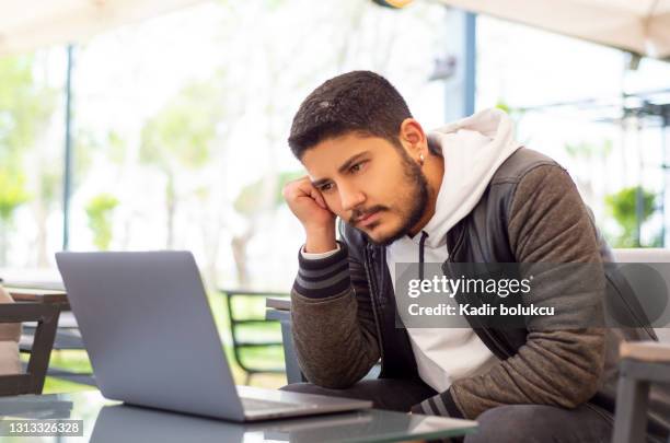 junger mann, der im café sitzt, schaut pessimistisch auf seinen computerbildschirm inmitten emotionalen stresses. - kündigungsfrist stock-fotos und bilder