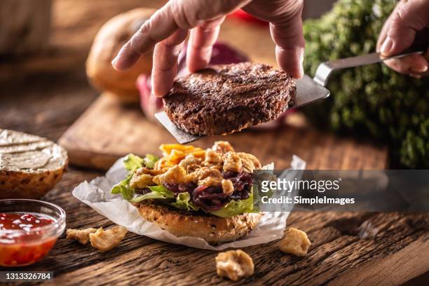 a cook finally assembling with spatula a lovely beef burger served with lettuce mayo, chilli dip and chicken pieces. - burger on grill photos et images de collection