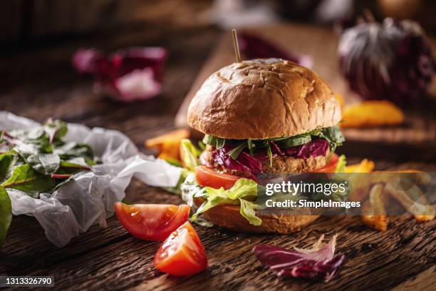 healthy veggie burger with vegan patty, fresh tomatoes, lettuce and potatofries served on wooden desk. - vegan food stock pictures, royalty-free photos & images