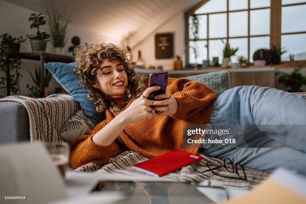 Woman using smart phone for social media laying in her couch