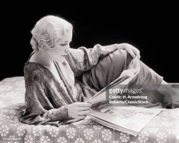 1930s Peroxide Blond Woman Wearing Silk Robe Lounging On Bed Reading Newspaper .