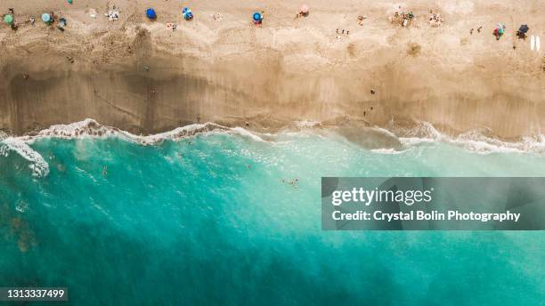 panoramica aerea diretta di una vibrante costa dell'oceano verde acqua e ombrelloni colorati su giove, in florida a metà giornata durante covid-19 nell'aprile del 2021 - jupiter florida foto e immagini stock