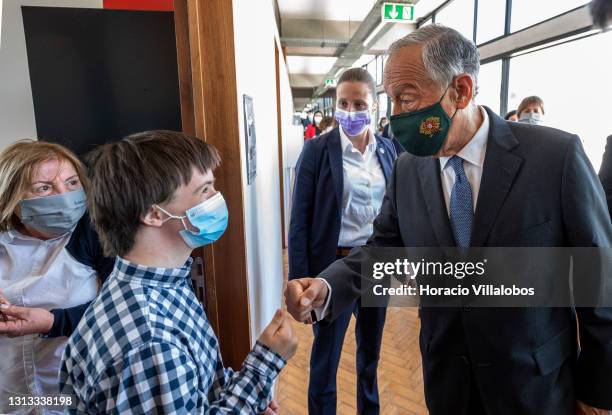 Portuguese President Marcelo Rebelo de Sousa wears a protective mask as he salutes a student during his visit accompanied by the Minister of...