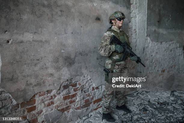 vrouwelijke huurling in camouflageuniform holdingsgeweer in oorlogsgebied - soldatenhelm stockfoto's en -beelden